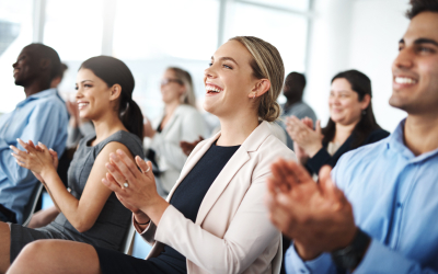 A group of people sitting in rows, clapping and smiling during an event.